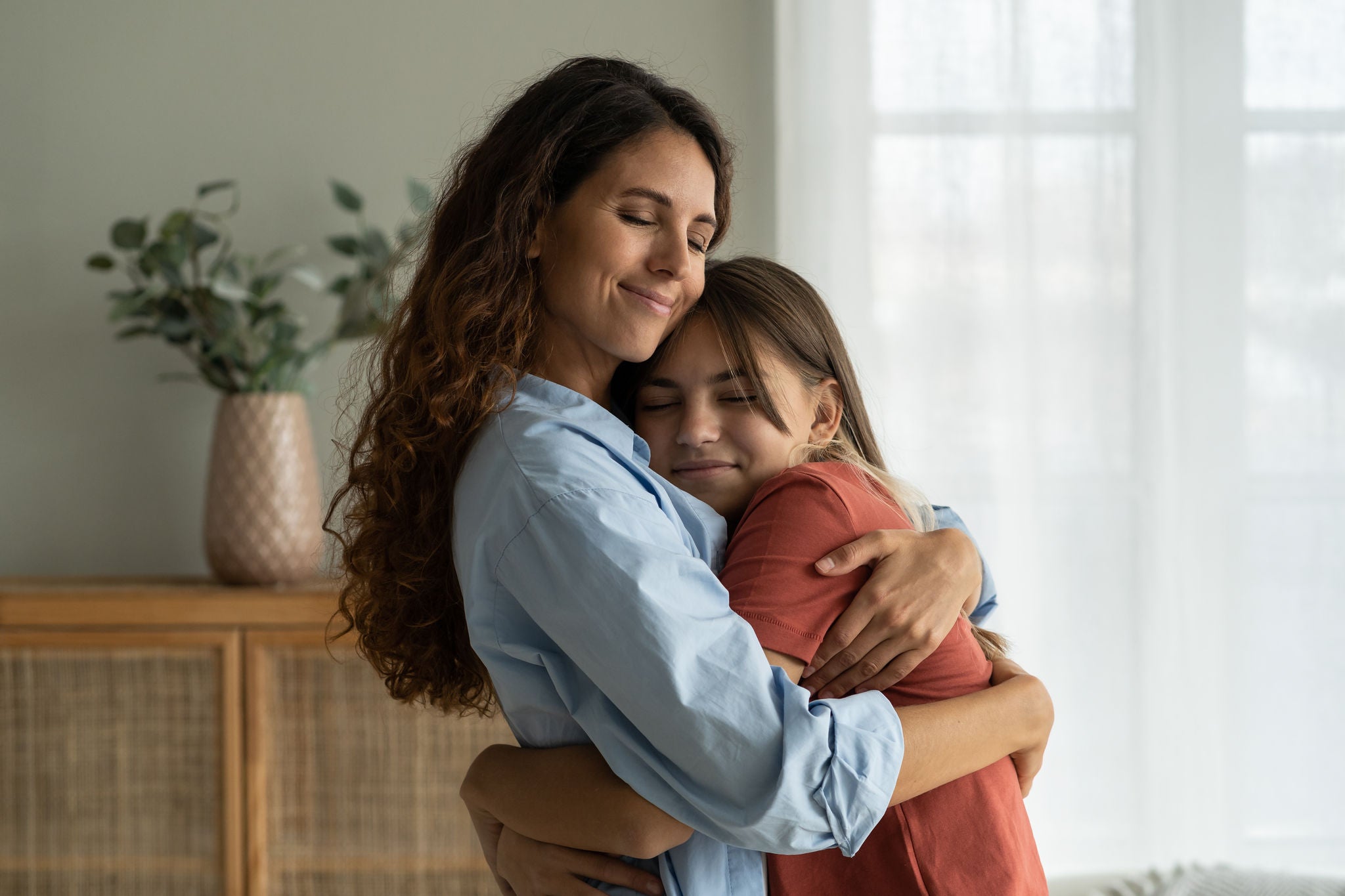 Young loving mother hugging her teenage daughter, mom demonstrating unconditional love for child, mommy cuddling supporting upset teen girl while spending time together at home. Mother-daughter bond 