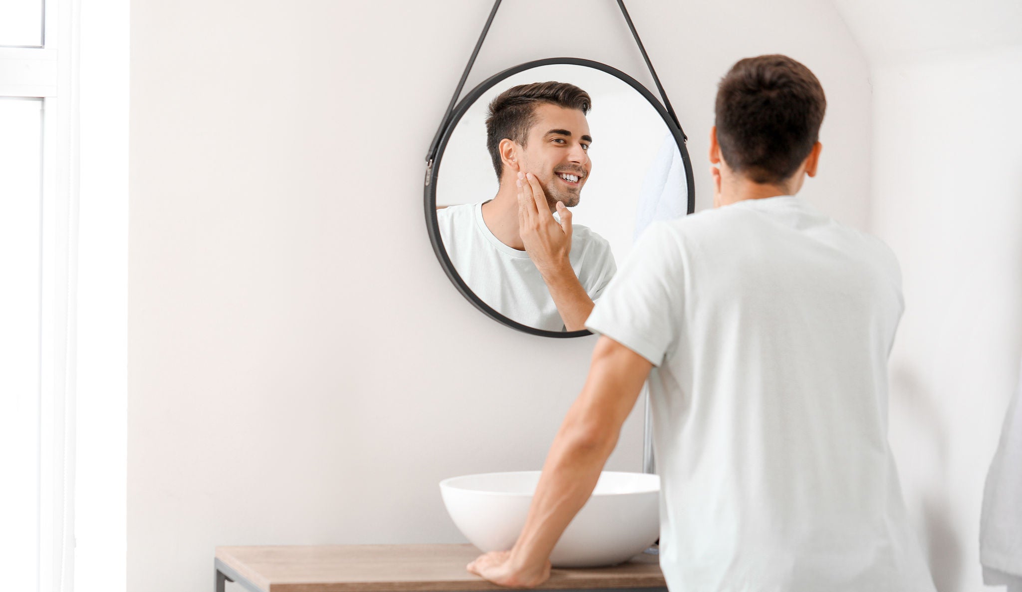 Man smiles at himself in mirror while touching his jaw.