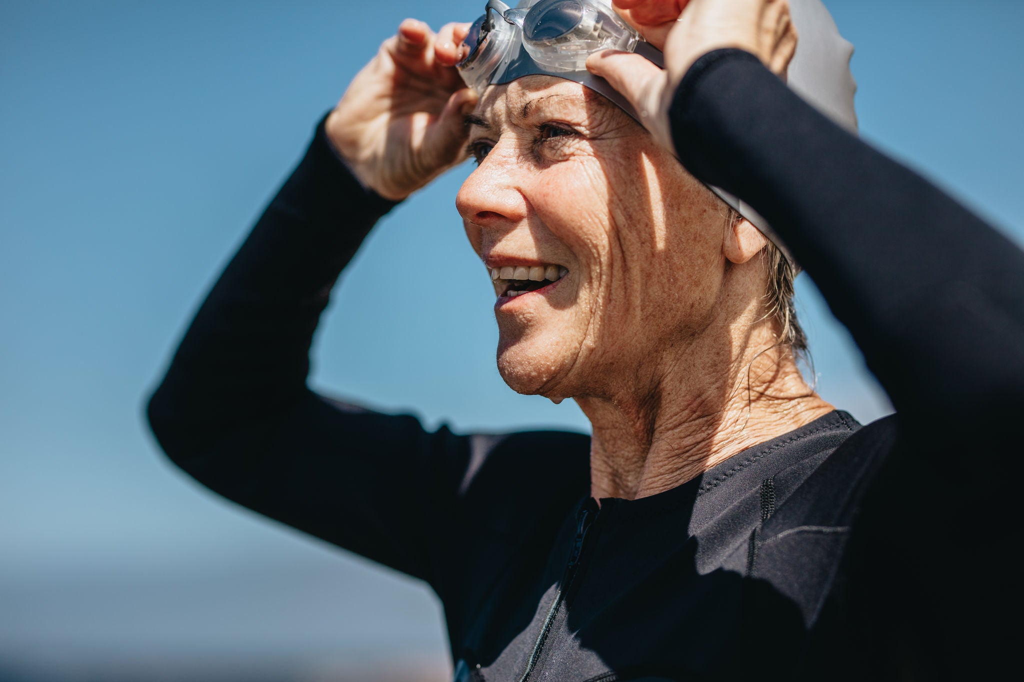 Portrait of a smiling senior woman in swimming costume standing outdoors. Senior woman taking off her swimming goggles after a swim.