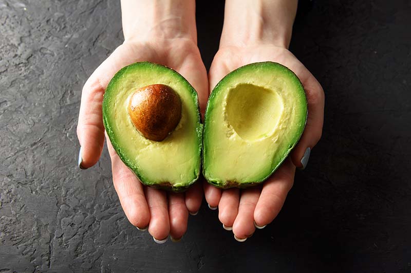 A woman holds a freshly cut avocado.