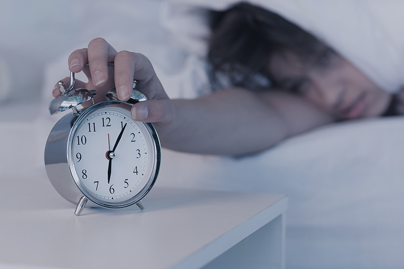 Woman hits snooze button on alarm clock after sleeping in.