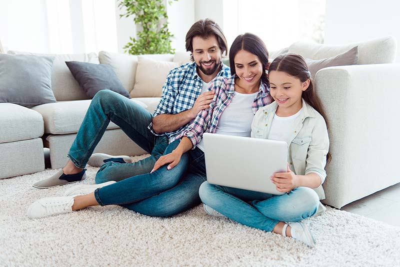 Parents and child with computer on living room floor. 