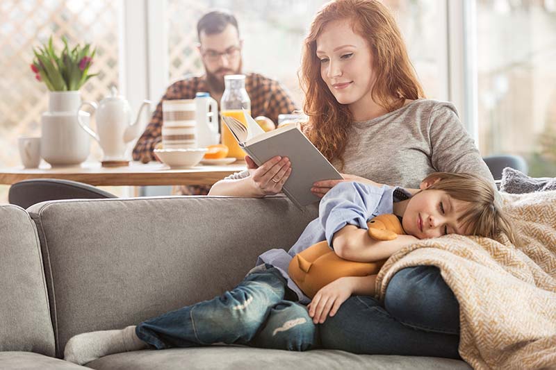 Mother reading book to son in living room.