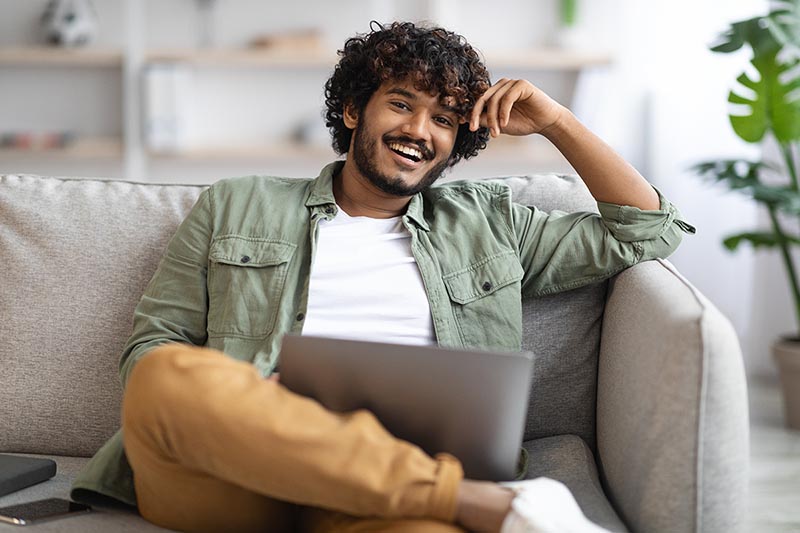 Man sitting on couch, looking at computer and enrolling in health insurance.