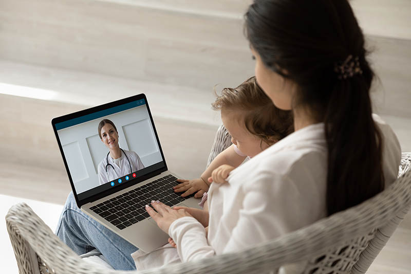 Woman completing a virtual doctor visit with a child on her lap.