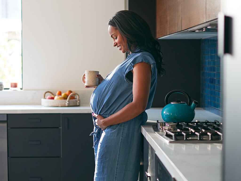 Pregnant woman holds coffee mug in kitchen