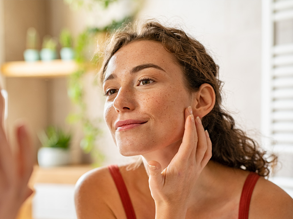 A young woman looks at her face in the mirror.
