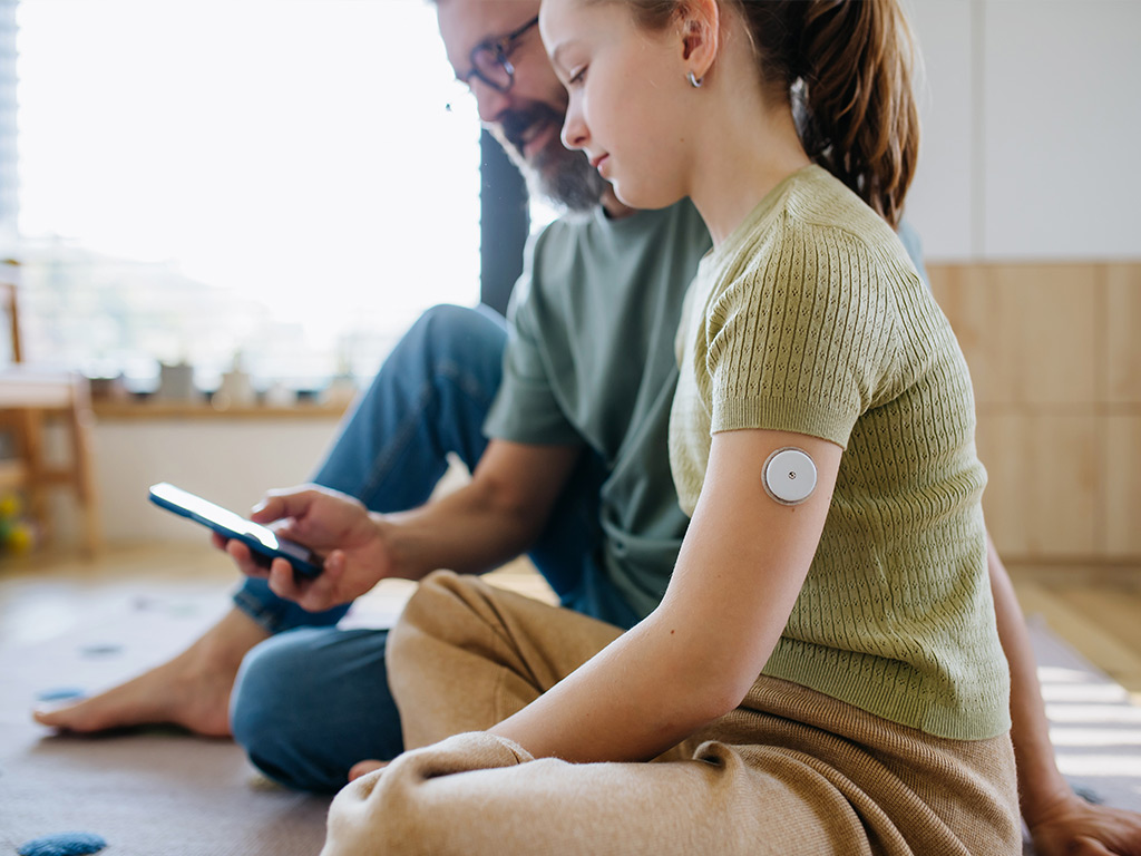 Photo of a dad helping his daughter check her blood sugar levels with CGM sensor and mobile app