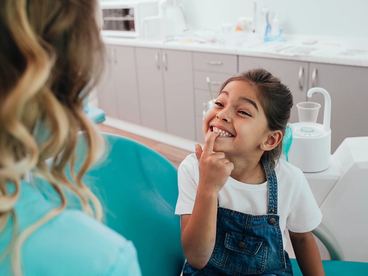 Mixed race little patient showing her perfect toothy smile while sitting dentists chair