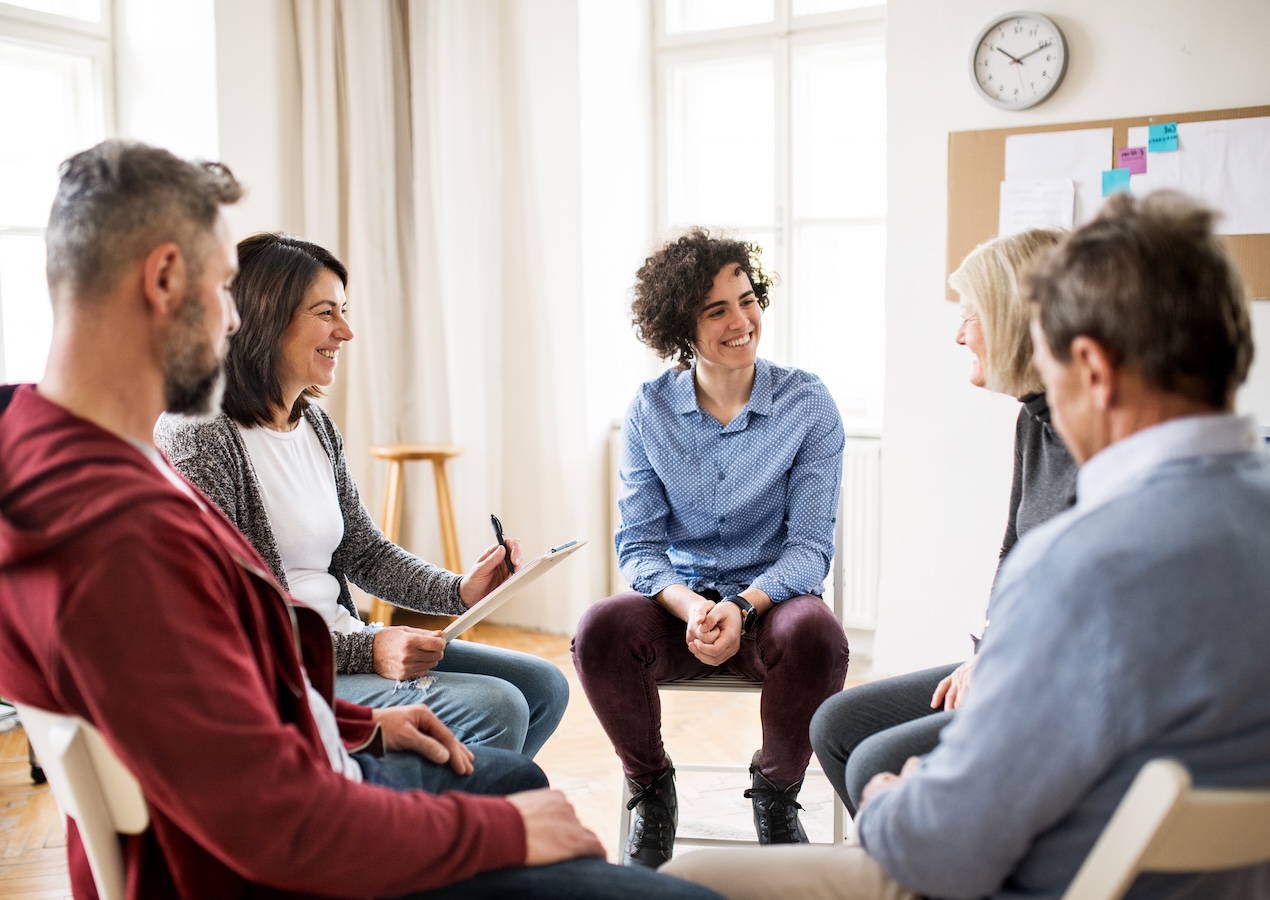 Men and women sitting in a circle during group therapy, talking.