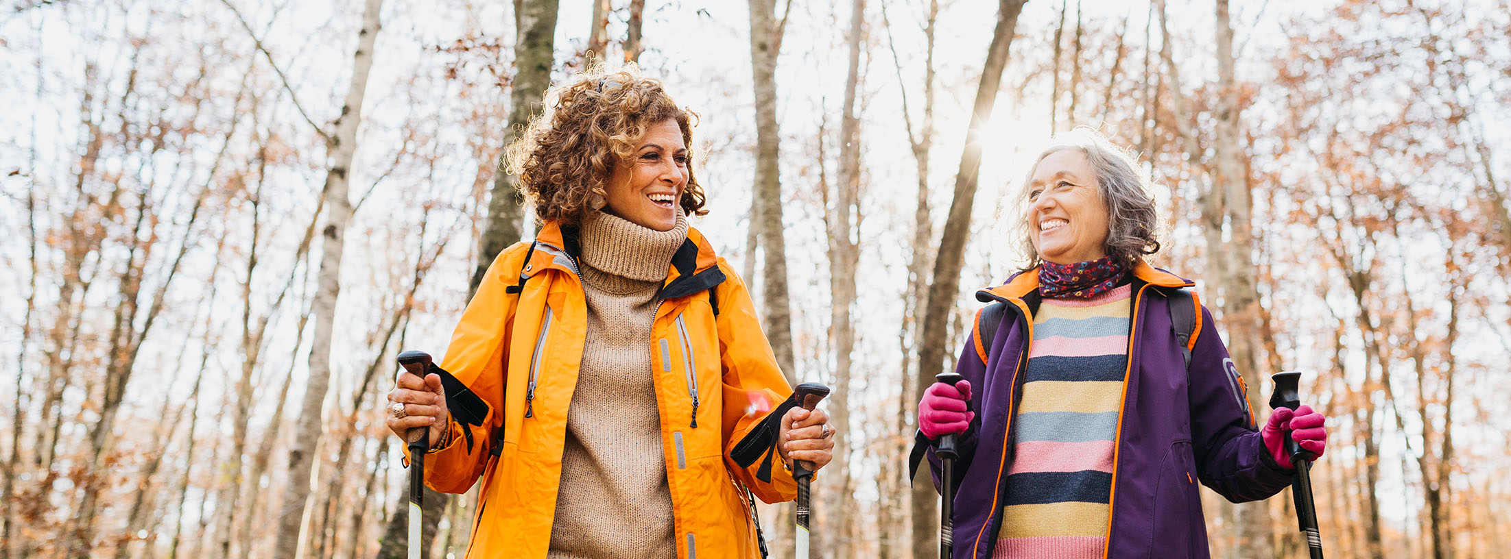 Two senior female friends hiking together through the forest in autumn