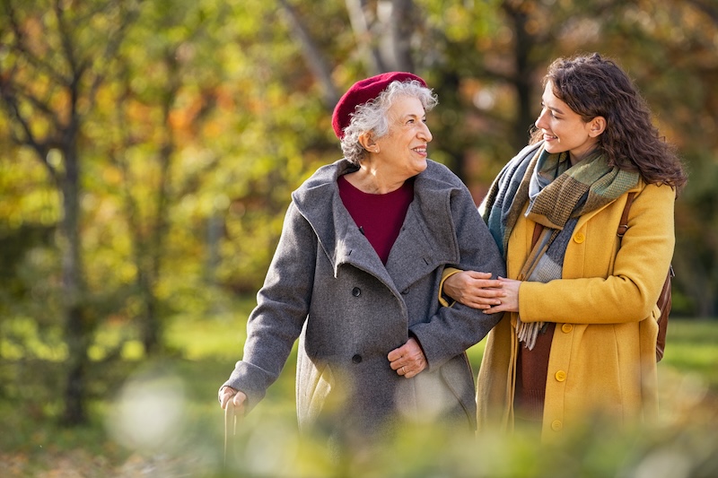 an elderly woman and a young woman walking together outdoors in the park