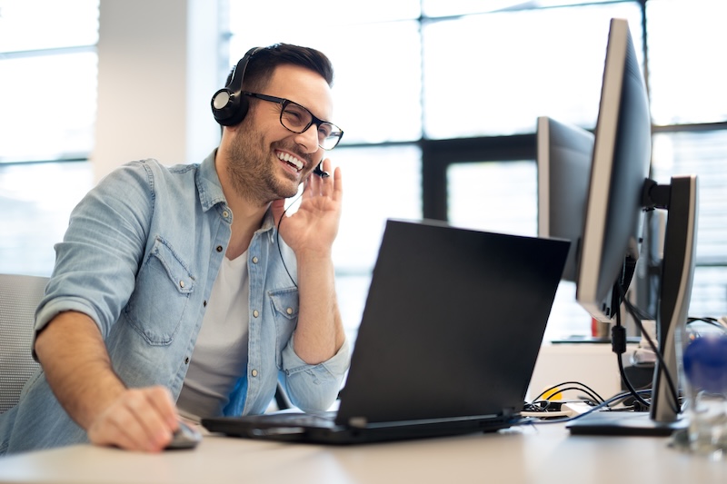 Man with a phone headset laughing at a computer