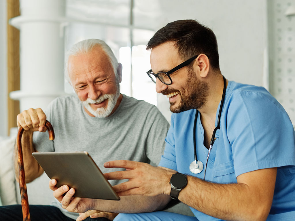 nurse doctor senior care tablet computer technology showing caregiver help assistence retirement home nursing elderly happy laughing man