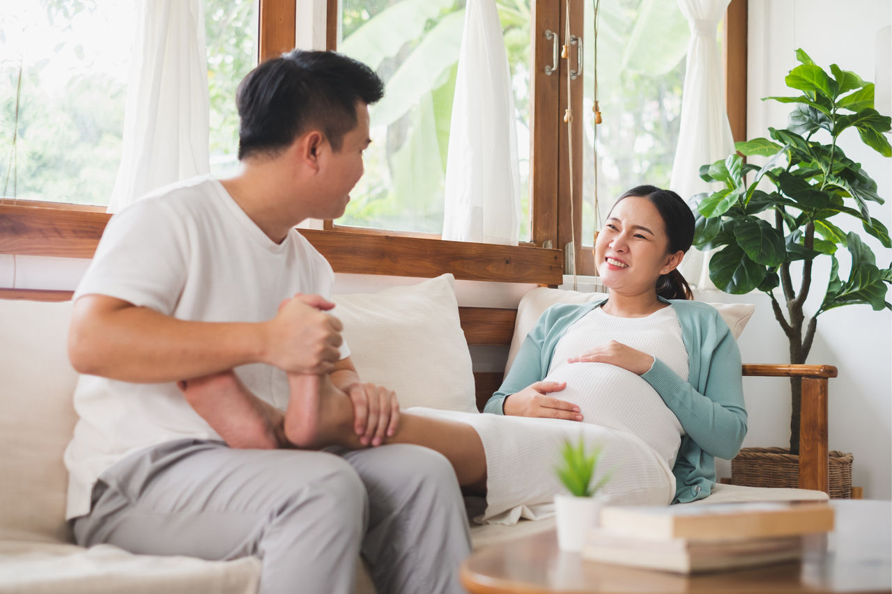 Asian young husband massaging pregnant wife feet at home, happy family