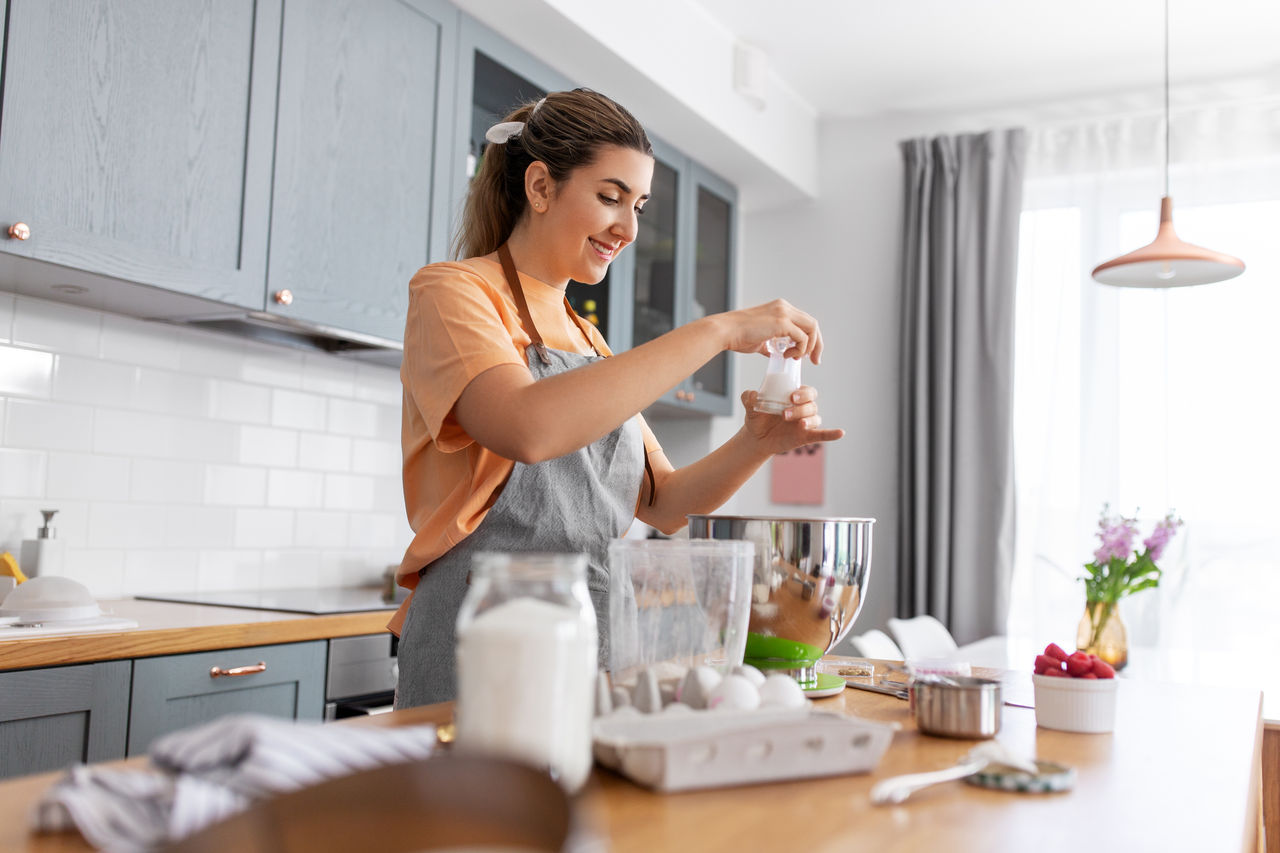 culinary, baking and people concept - happy smiling young woman cooking food on kitchen at home and adding salt