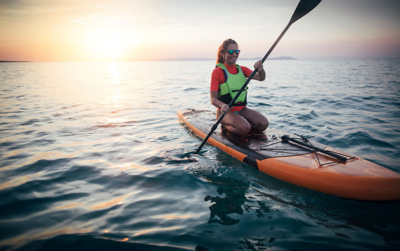 A woman practicing paddle on a sunset sea, copy space
