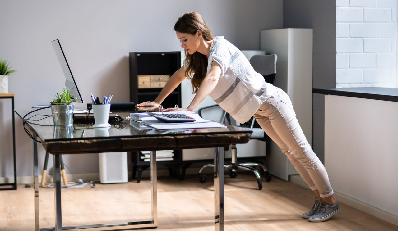 Side View Of A Young Businesswoman Doing Push Up On Office Desk