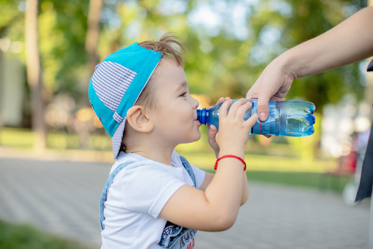 a little boy in a cap with a smile drinking water from a bottle in the Park