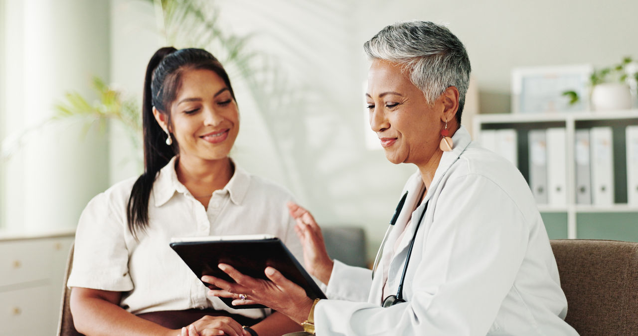 Smile, women and doctor on tablet in office for good news, research and online results of diagnosis. People, digital and consultation of healthcare, insurance checklist and treatment plan and medical.