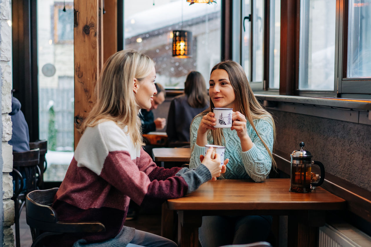 Two women drink coffee in a cozy bar and have a friendly conversation.