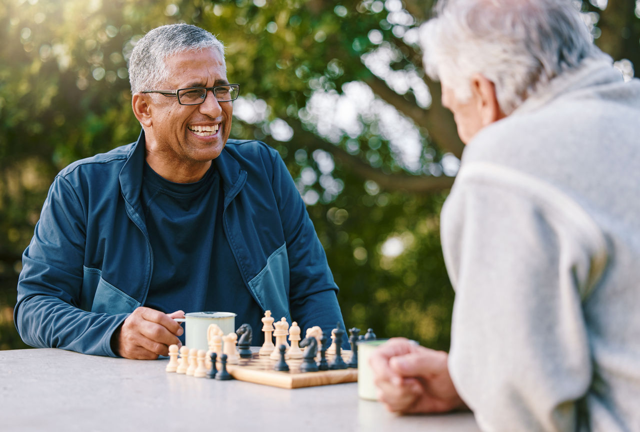 Chess, nature and retirement with senior friends playing a boardgame while bonding outdoor during summer. Park, strategy and game with a mature man and friend thinking about the mental challenge.