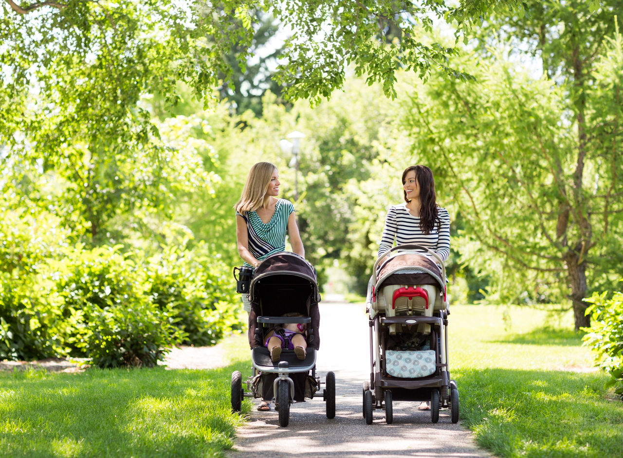 Happy mothers with their baby carriages walking together in park
