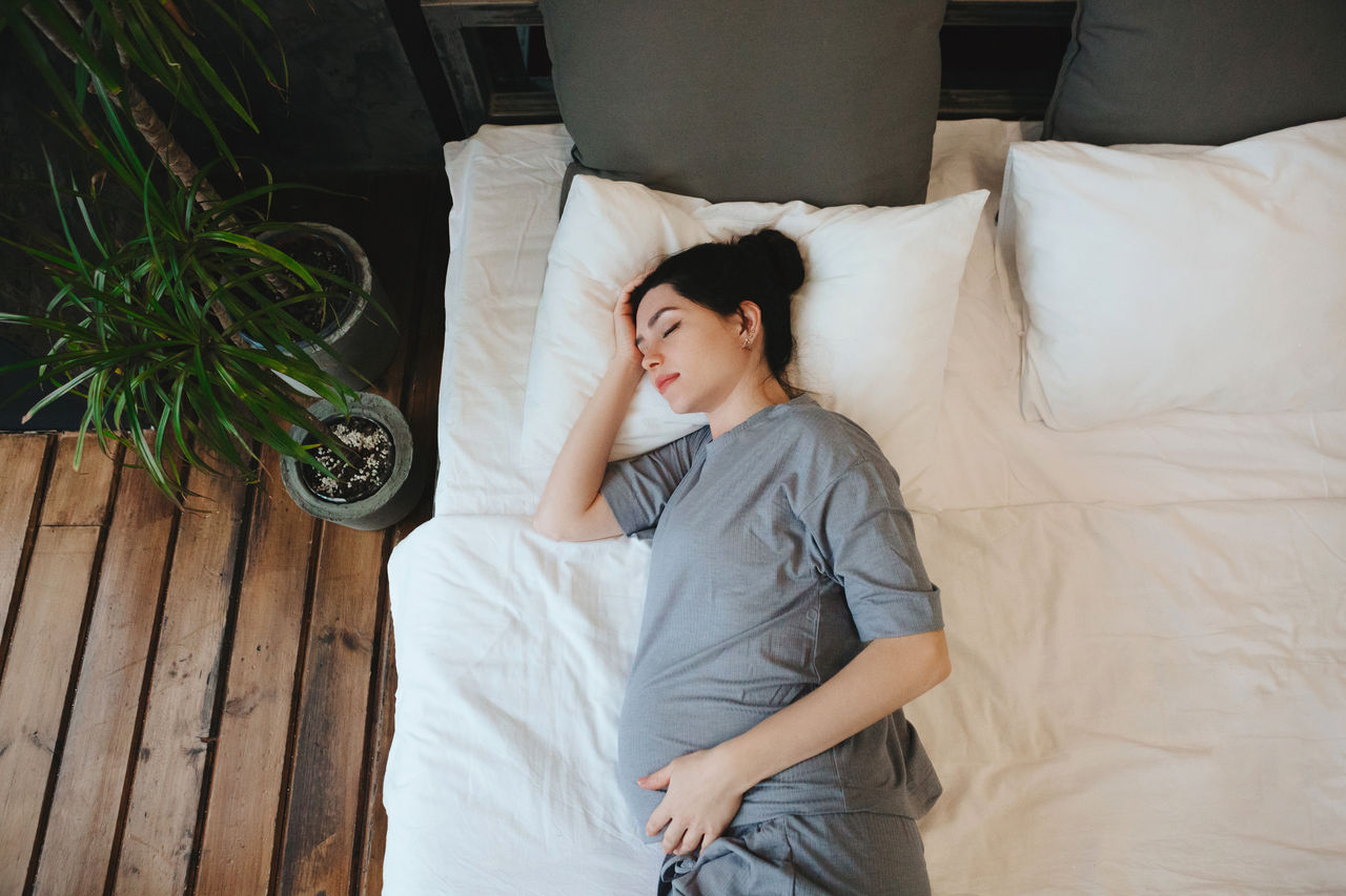 View from above of pregnant woman relaxing resting on couch at home, expectant mother lying on the bed holding belly touching tummy, cropped shot. Pregnancy, maternity and prenatal period concept