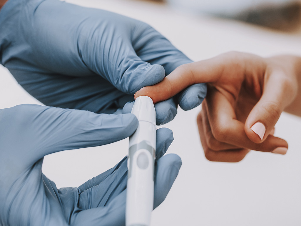 Gloved medical professional uses blood sugar test on a woman's finger.