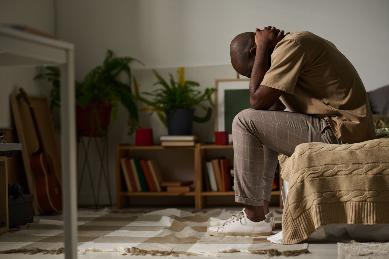 African American young man sitting on bed in depression and worried about his problems