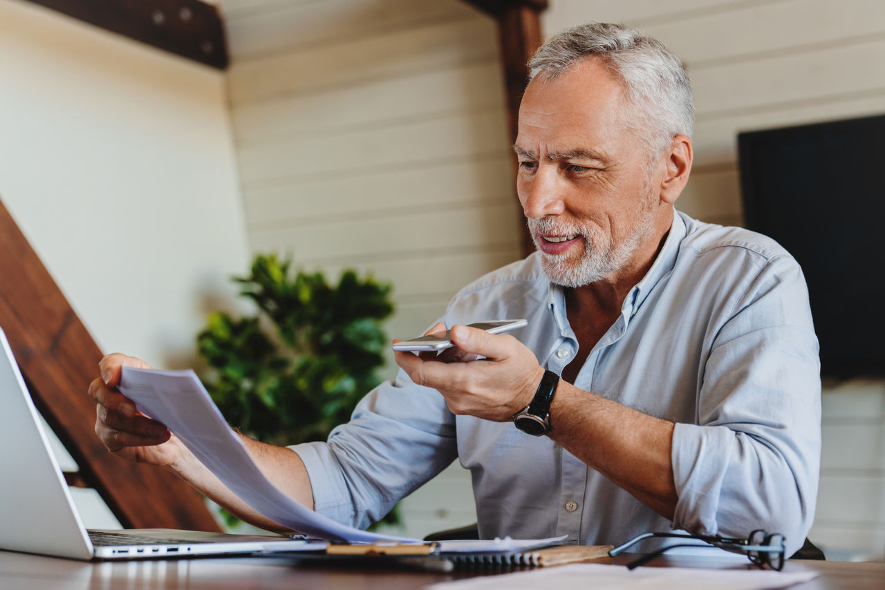 Senior man working at home while discussing using speakerphone Senior man working at home while discussing using speakerphone