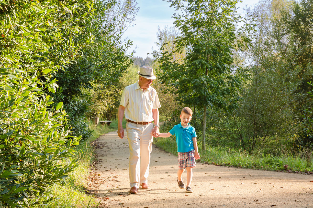 Front view of grandfather with hat and grandchild walking on a nature path